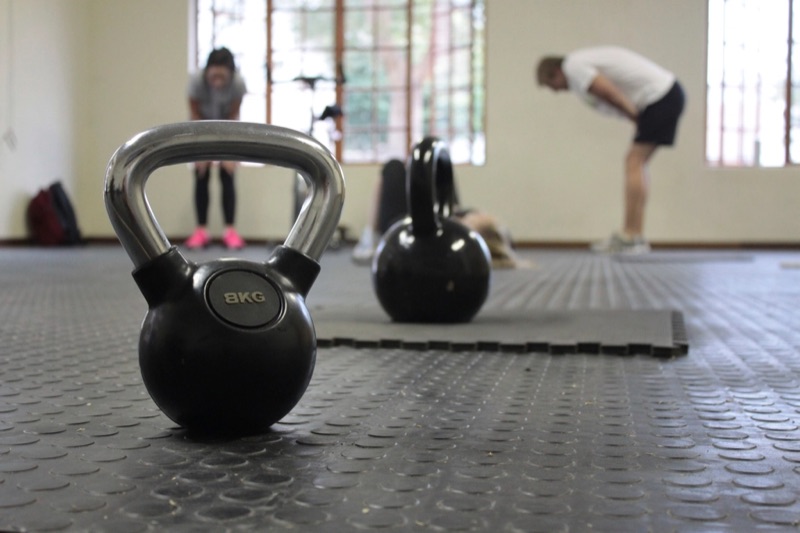 Kettlebells on a rubber gym floor with people training behind