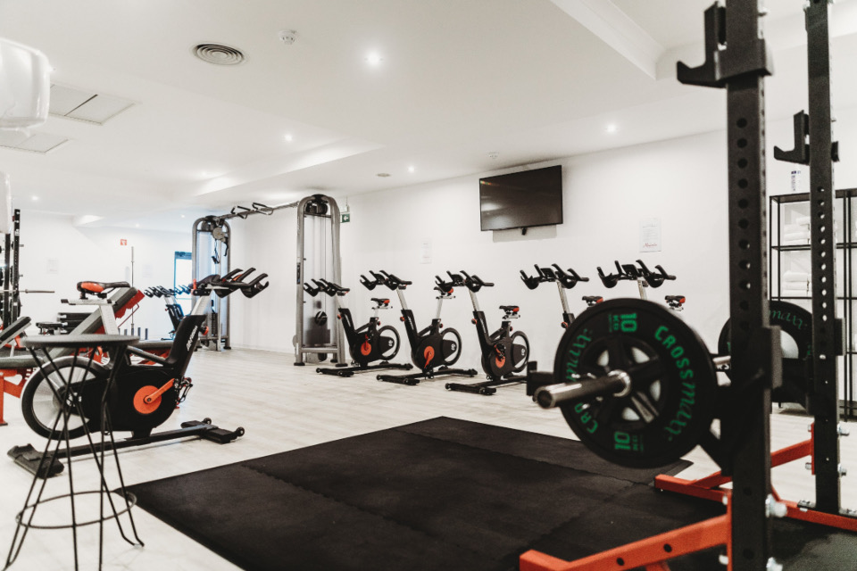 Bright gym floor with exercise bikes, a squat rack and weight plates