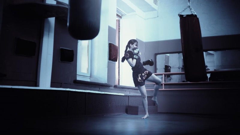 Coach throwing a kick beside a heavy bag in a boxing gym